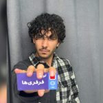 تصویر یک پسر که کارت در دست دارد و مدل مو او فر است.